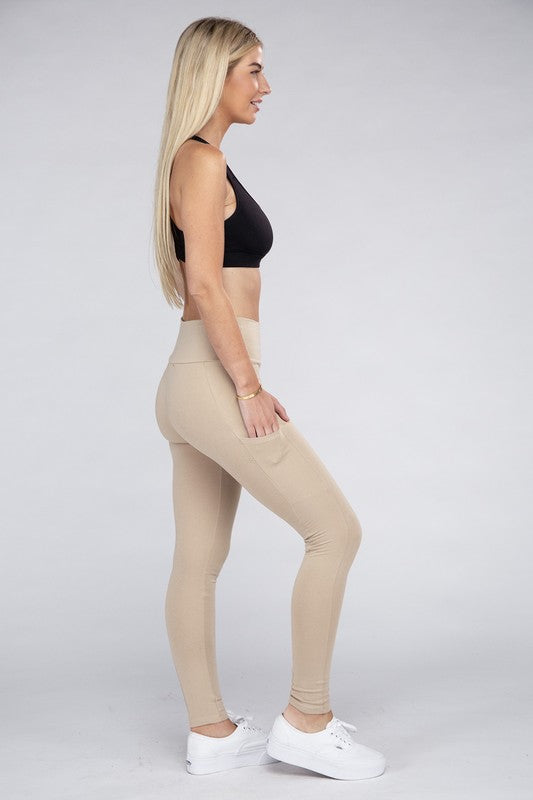 A person is wearing high-waisted dark gray Active Leggings Featuring Concealed Pockets, a bracelet on their left wrist, and white sneakers. The background is a plain light gray.