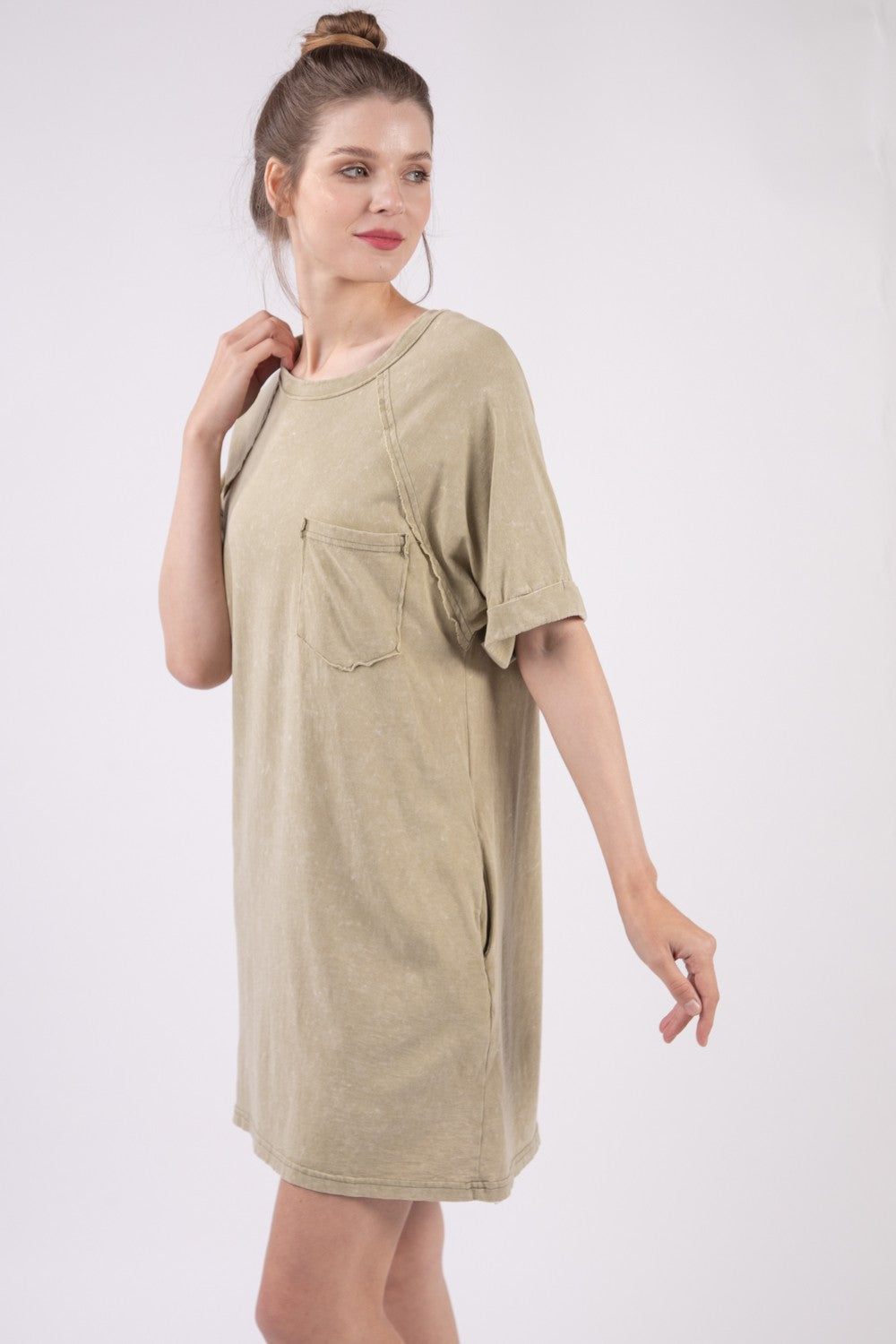 A woman in a VERY J Washed Round Neck Mini Tee Dress poses gracefully against a plain background. Her casual ensemble features an oversized beige tee dress complete with a pocket, radiating effortless style and comfort.