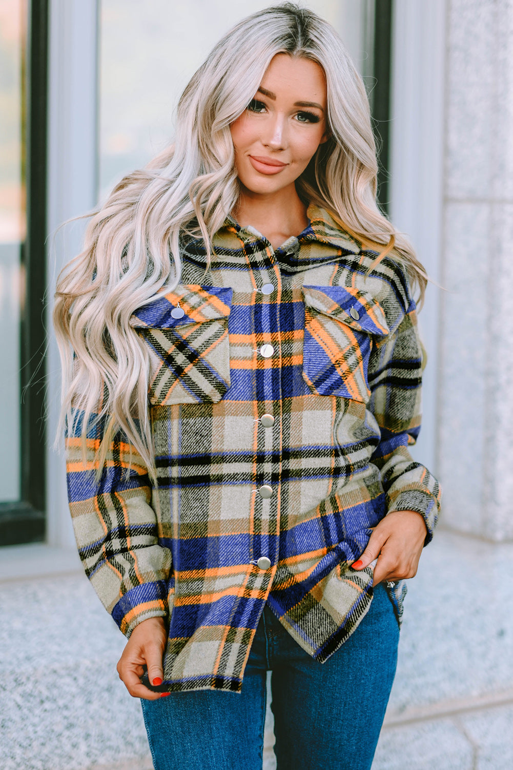 A person wearing a Brown Plaid Button Up Long Sleeve Flannel Shacket layered over a white top with ripped jeans and holding a brown handbag stands against a textured gray wall.