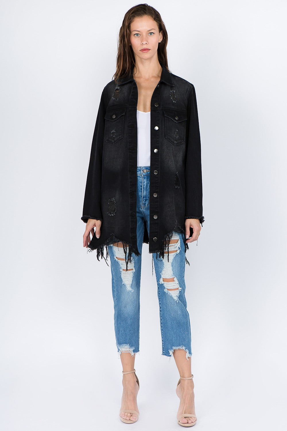 A woman wearing the American Bazi Distressed Frayed Hem Denim Jacket over a white top and ripped blue jeans stands against a plain background, giving her outfit a vintage feel.