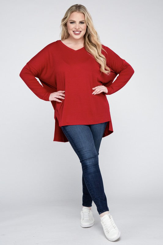 A woman with long, blonde hair wears a Plus Dolman Sleeve V-Neck Side Slit Hi-Low Hem Top and blue jeans, posing with one hand on her hip and smiling at the camera.