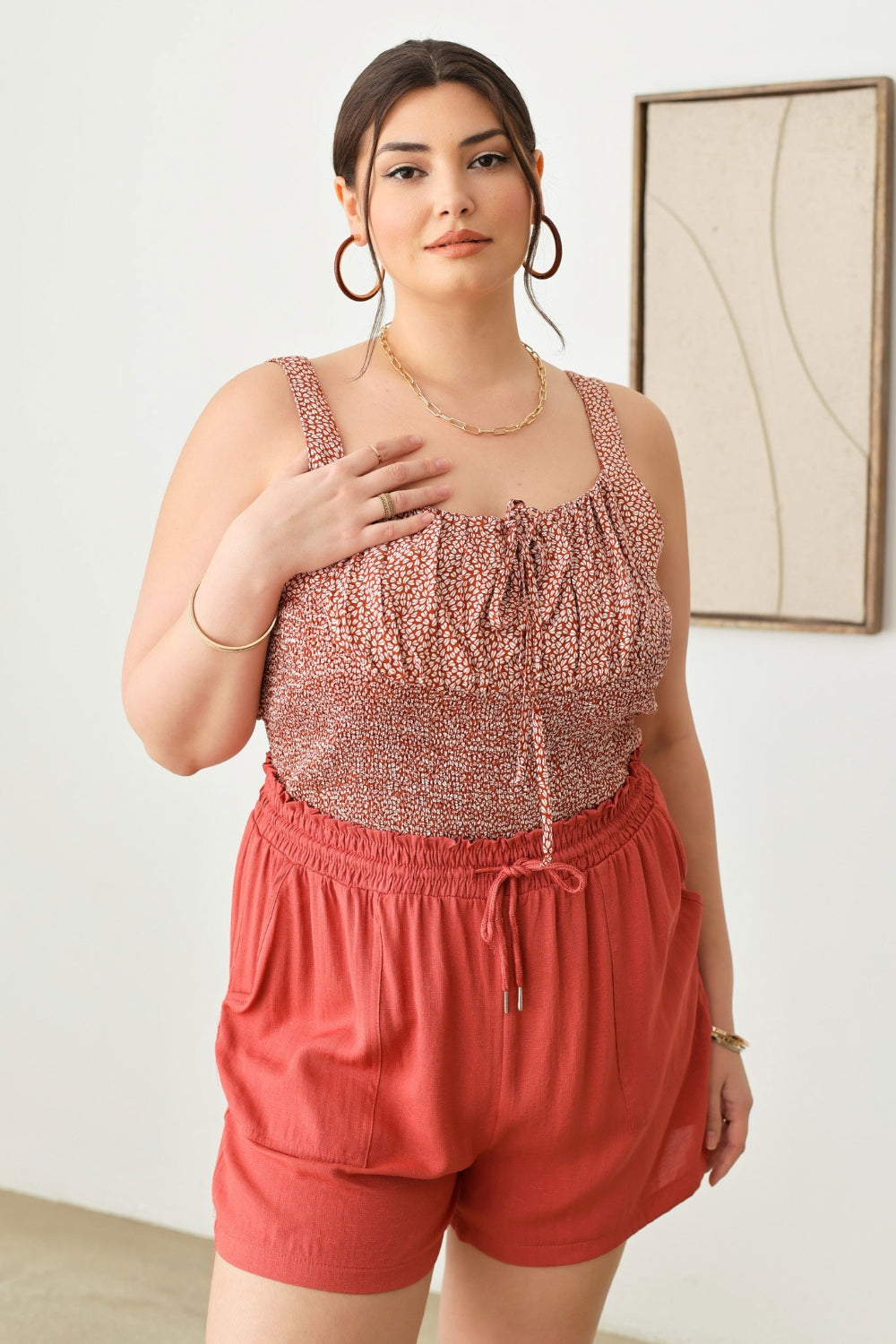 A woman wearing a light green cut-out top and Zenobia Plus Size Drawstring Elastic Waist Shorts with Pockets stands indoors, holding a woven handbag.