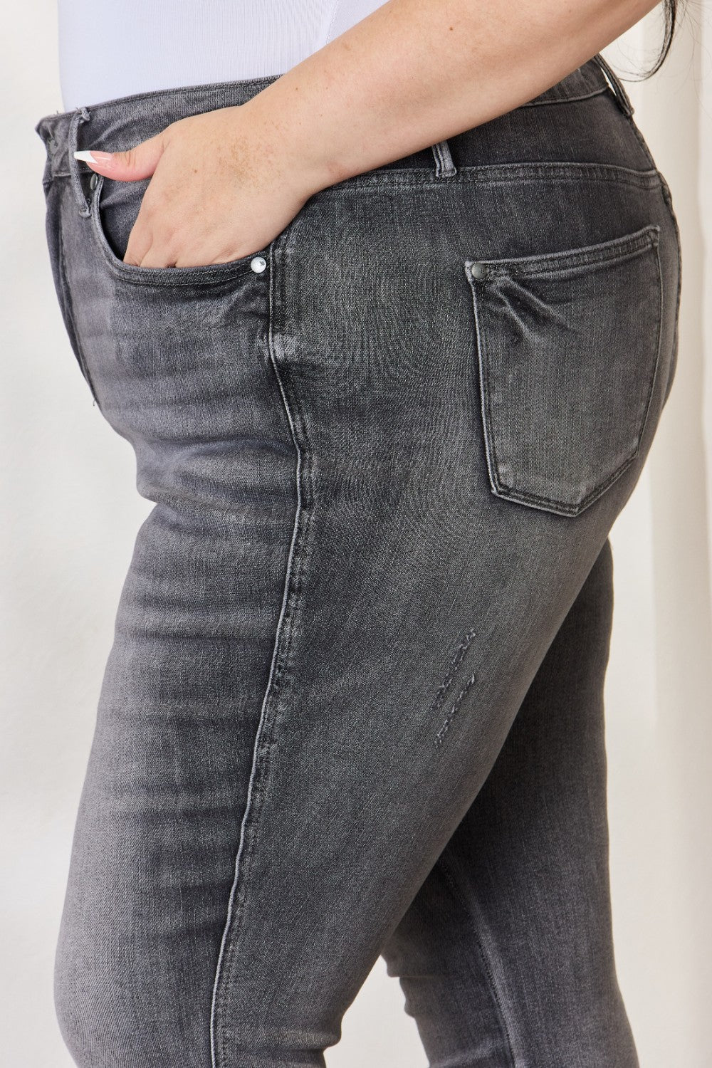 A person wearing the Judy Blue Full Size High Waist Tummy Control Release Hem Skinny Jeans paired with nude heels stands against a light background.