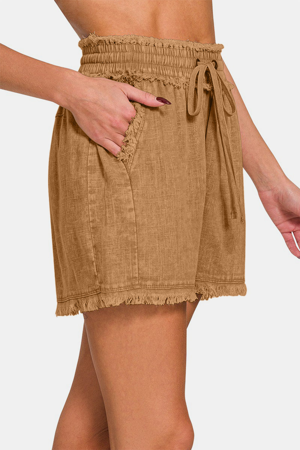 A person is wearing the Zenana Washed Linen Frayed Hem Drawstring Shorts, which come in a brown shade. These high-waisted shorts have a drawstring waist, frayed hem, and practical side pockets.