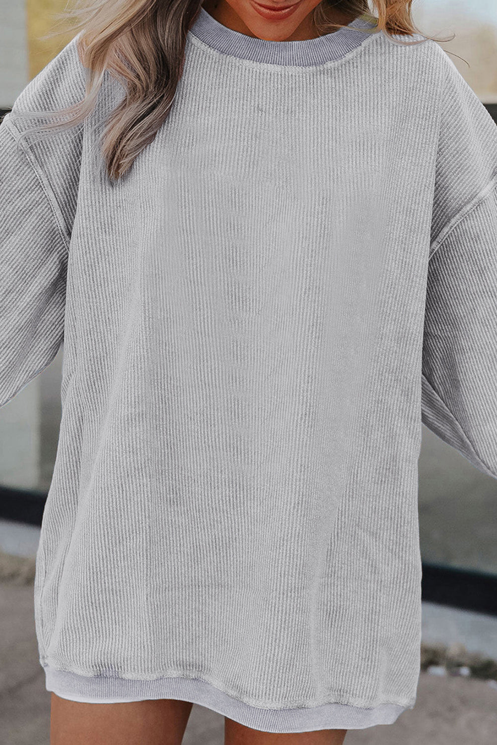 A woman wearing the Light Grey Ribbed Corduroy Oversized Sweatshirt with loose long sleeves, designed in corded fabric, making it fashionable for all body shapes.