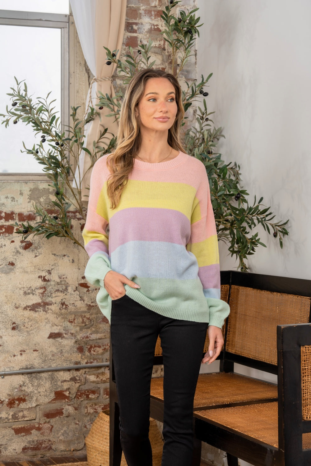 A woman wearing the Sew In Love Full Size Color Block Round Neck Dropped Shoulder Sweater stands indoors next to a chair and potted plant.