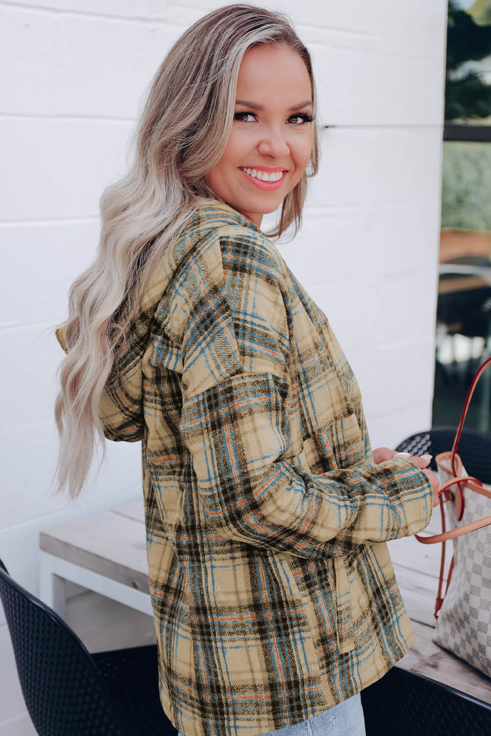 A person with long blonde hair, seen from the back, wearing a Khaki Plaid Button Neck Pocketed Pullover Hoodie and denim shorts, stands on a porch.