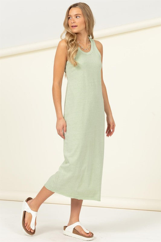 A woman dressed in a Fun Day Sleeveless Shift Midi Dress, light green and ankle-length, stands against a light background. She pairs the outfit with white sandals and a necklace.