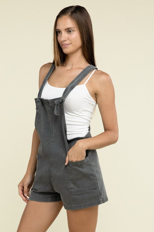 A person wearing the Washed Knot Strap Romper and a white tank top stands against a plain background.