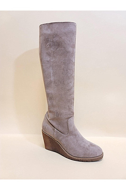 A single NAVAEH-WEDGES knee-high boot with a beige suede finish and a wedge heel, positioned upright against a plain background.