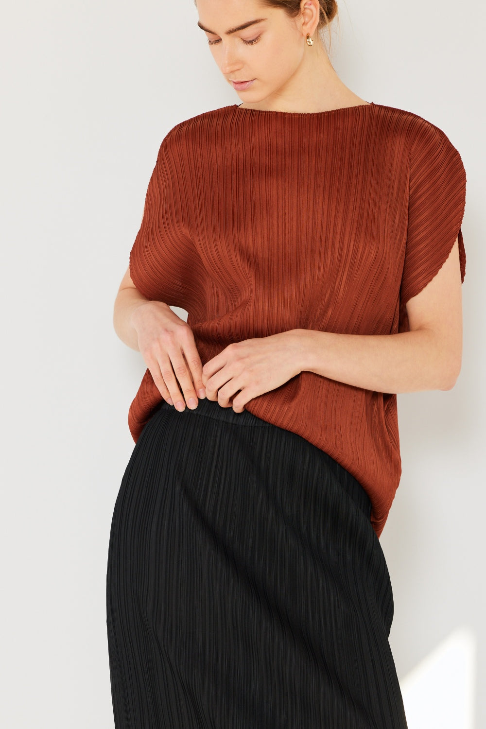 A person wearing the Marina West Swim Rib Pleated Oversized Dolman Sleeve Top in a fashionable light blue shade, paired with a brown belt and black skirt, stands against a plain background.