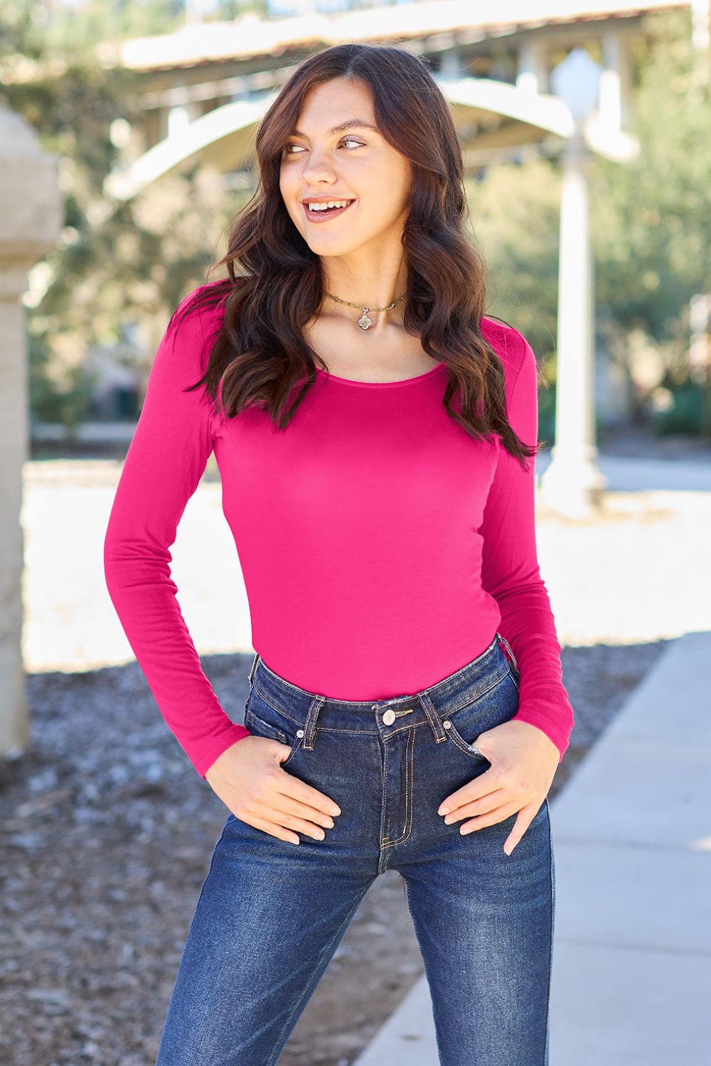 A person poses confidently in the Basic Bae Full Size Round Neck Long Sleeve Bodysuit, made from a rayon spandex blend, with one hand touching their neck and the other resting on their hip.