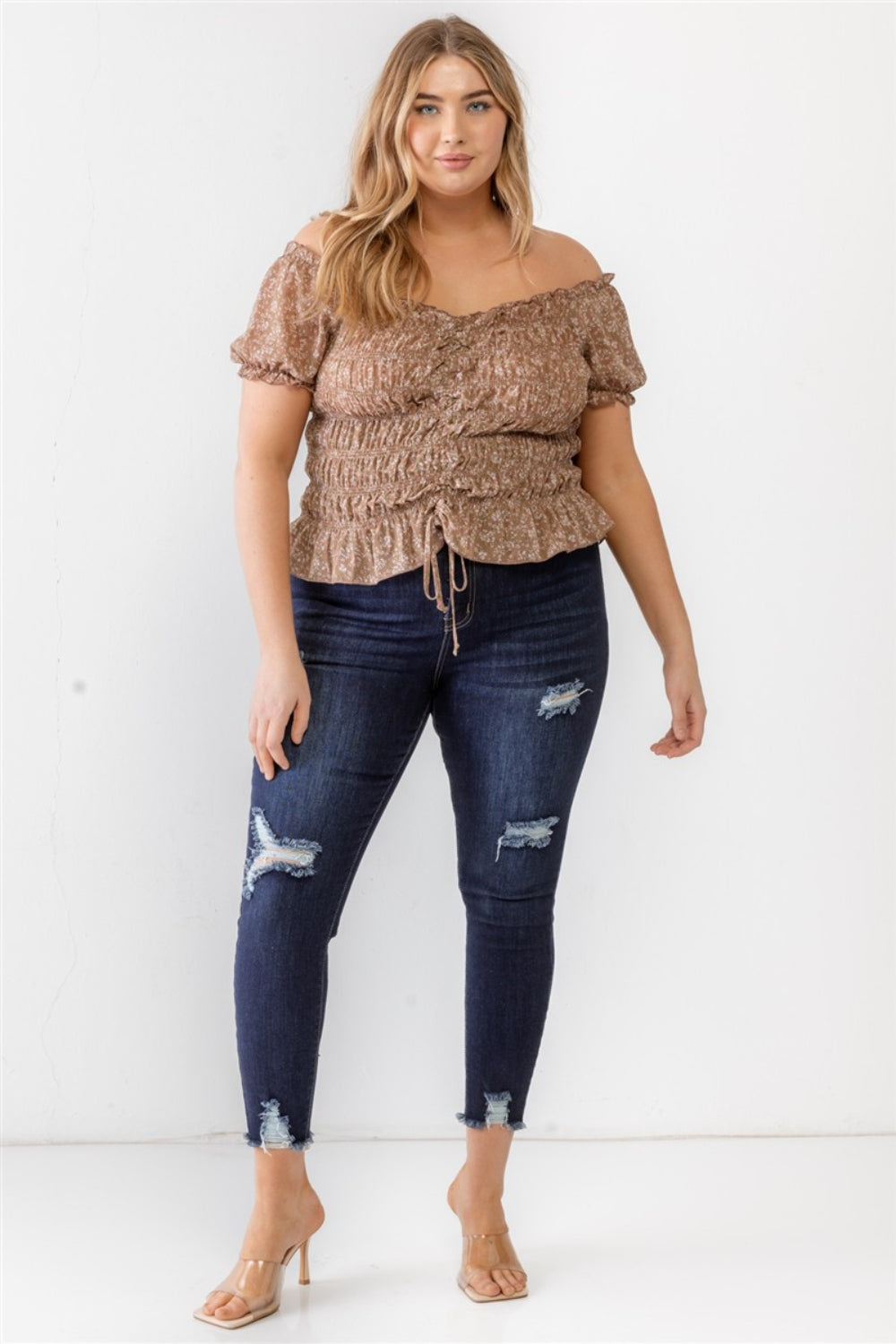 Wearing the Zenobia Plus Size Frill Ruched Off-Shoulder Short Sleeve Blouse and ripped jeans, a person with long hair poses against a plain white background.