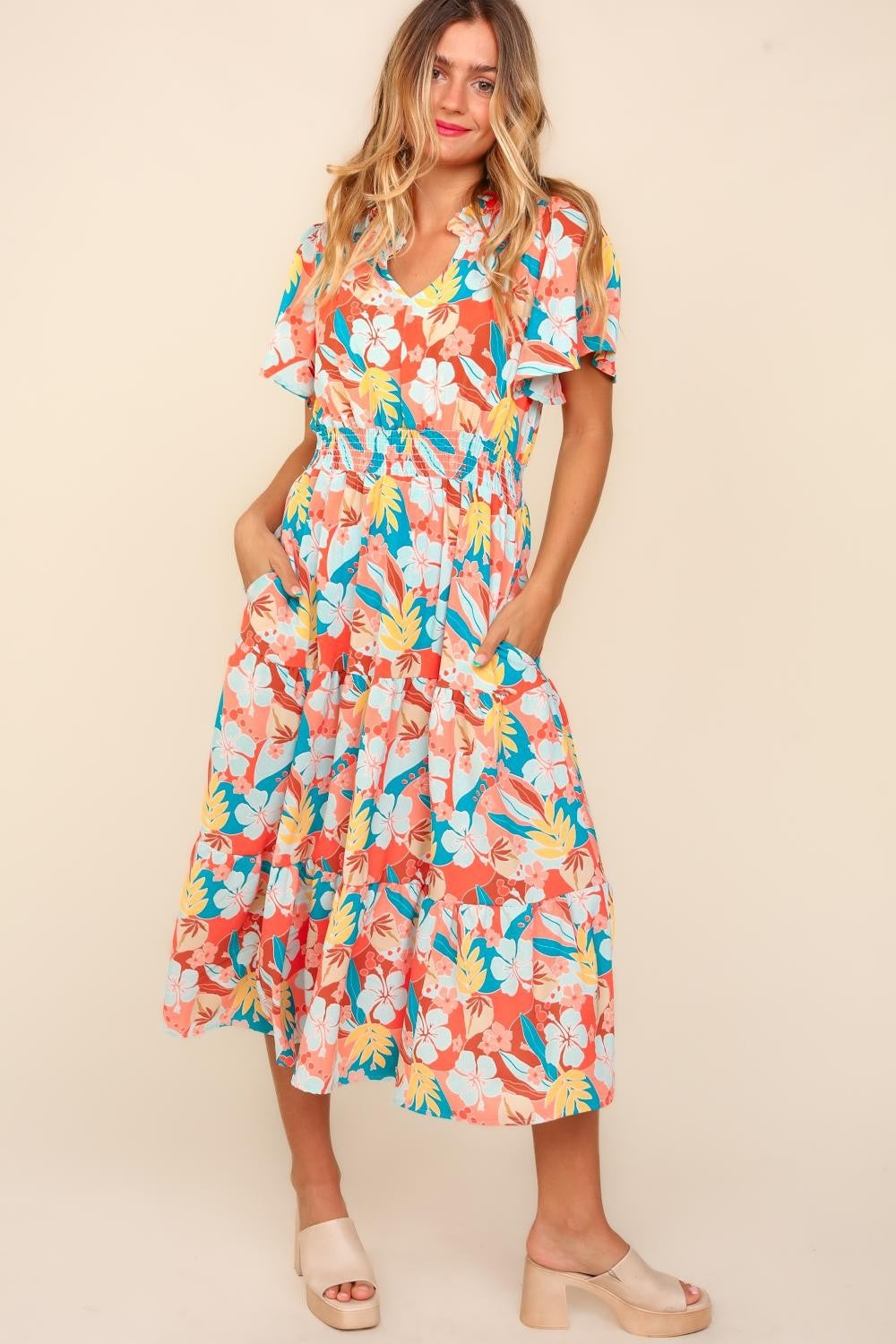 A person wearing the Haptics Full Size Tropical Floral Tiered Dress with Side Pockets and beige platform sandals stands against a plain background.