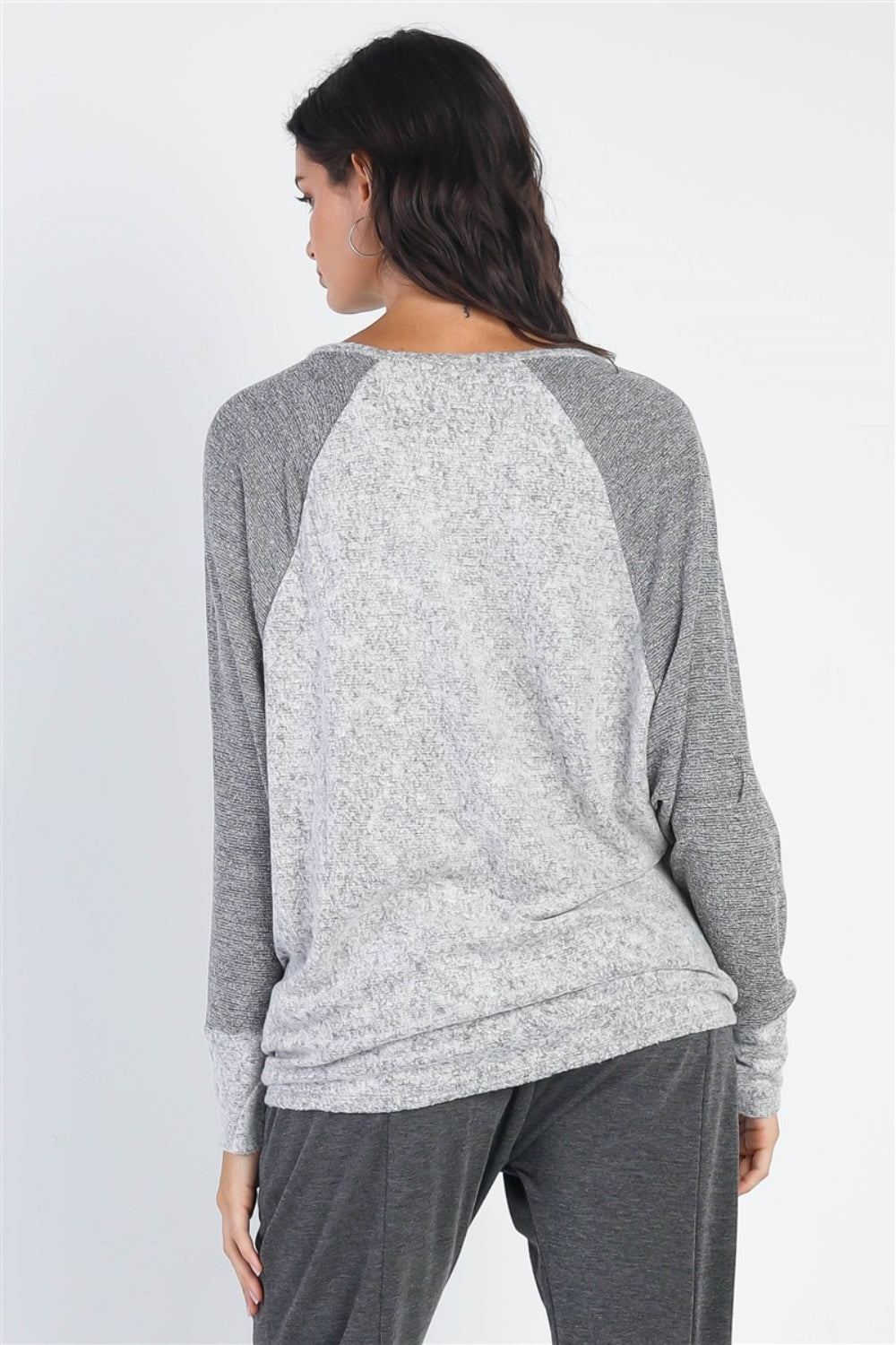 A woman stands wearing the Cherish Apparel Round Neck Long Sleeve Contrast Top in pink and gray with matching gray pants, set against a plain background.