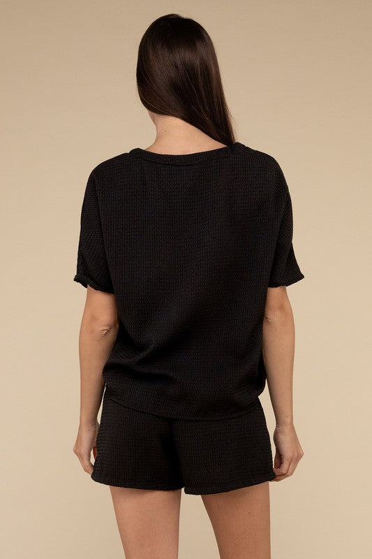 Clad in the Waffle Round Neck Top and Short Set paired with black sunglasses, a person stands against a plain beige background, highlighting the non-stretch polyester fabric.