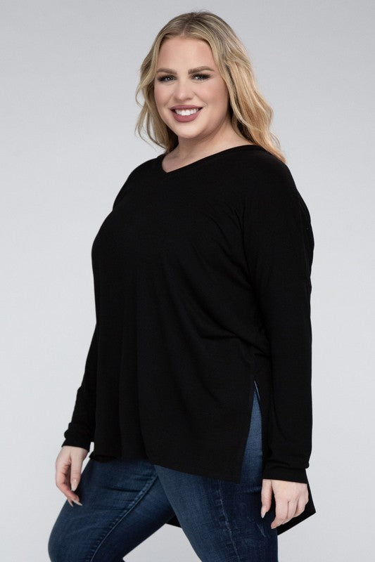 A woman with long, blonde hair wears a Plus Dolman Sleeve V-Neck Side Slit Hi-Low Hem Top and blue jeans, posing with one hand on her hip and smiling at the camera.