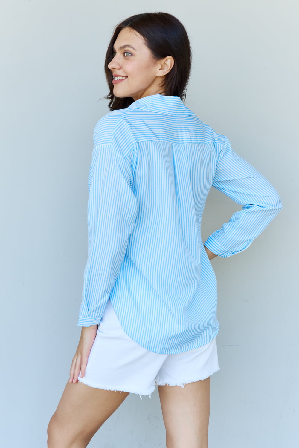 A person with long dark hair smiles while wearing the Doublju She Means Business Striped Button Down Shirt Top in light blue and white shorts, standing against a plain light background.