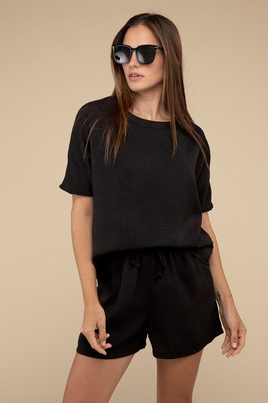 Clad in the Waffle Round Neck Top and Short Set paired with black sunglasses, a person stands against a plain beige background, highlighting the non-stretch polyester fabric.