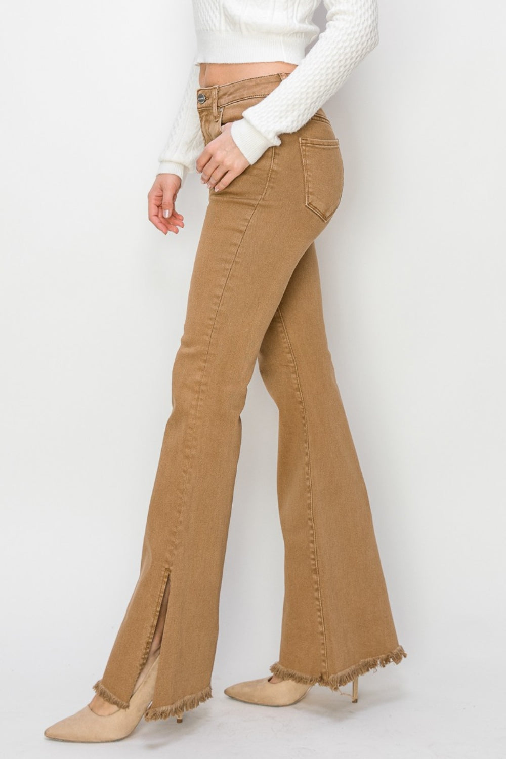 Wearing the RISEN Bailey Full Size High Waist Side Slit Flare Jeans with frayed hems, a person pairs them with beige boots against a white background.