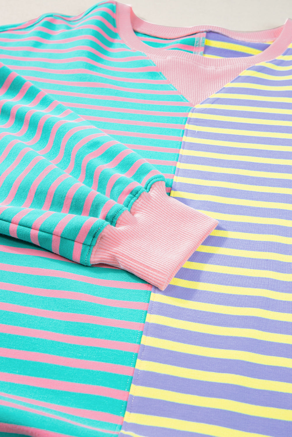 A person with wavy hair is seen from behind wearing a Casual Stripe Colorblock Drop Shoulder Oversize Sweatshirt in pastel colors and blue jeans. They are carrying a white shoulder bag, showcasing a trendy color block design.