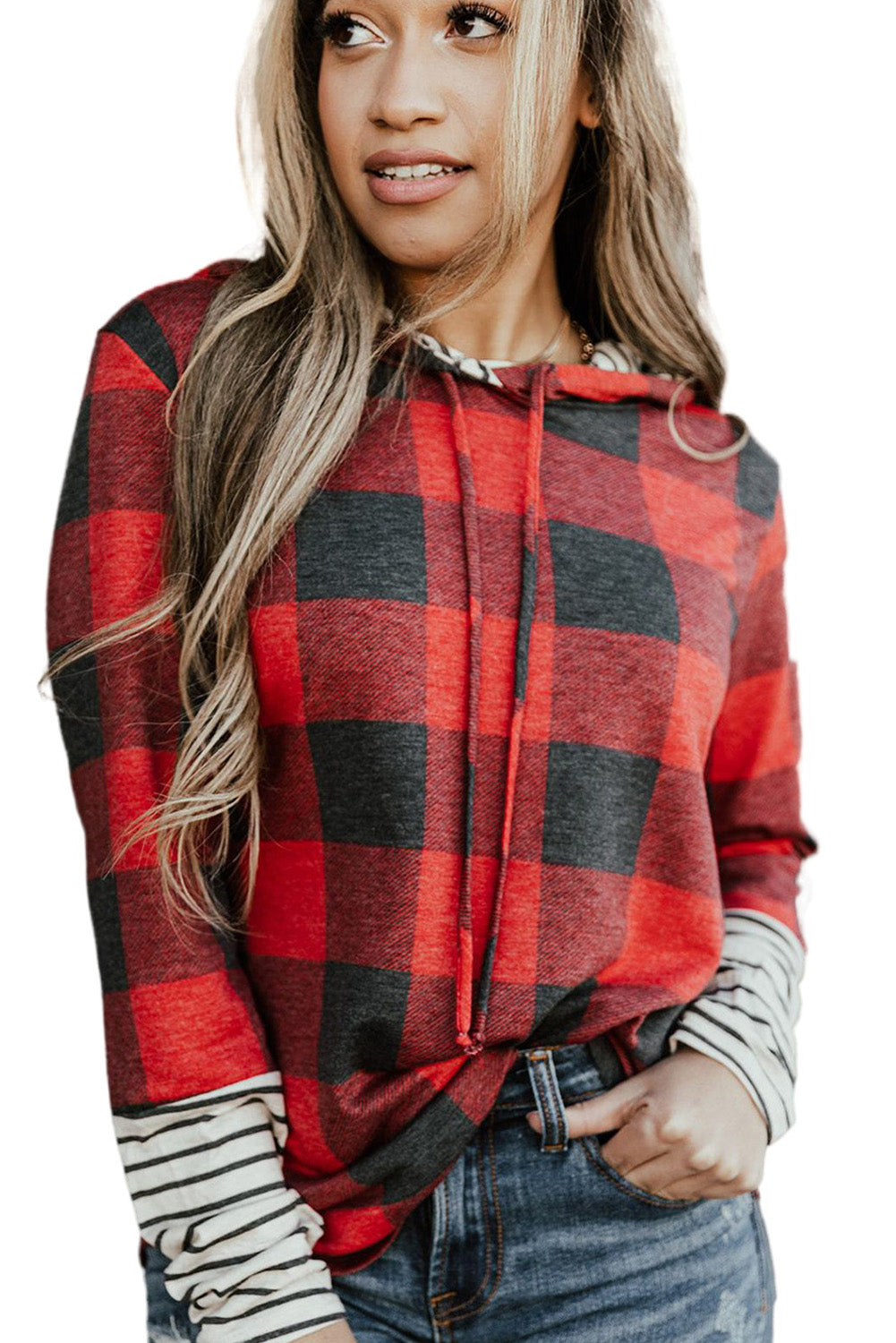 A person stands wearing the Fiery Red Christmas Plaid Striped Patchwork Drawstring Hoodie, characterized by its red and black plaid pattern with striped sleeves. They look to the side with one hand in their pocket, perfectly embodying a casual style.