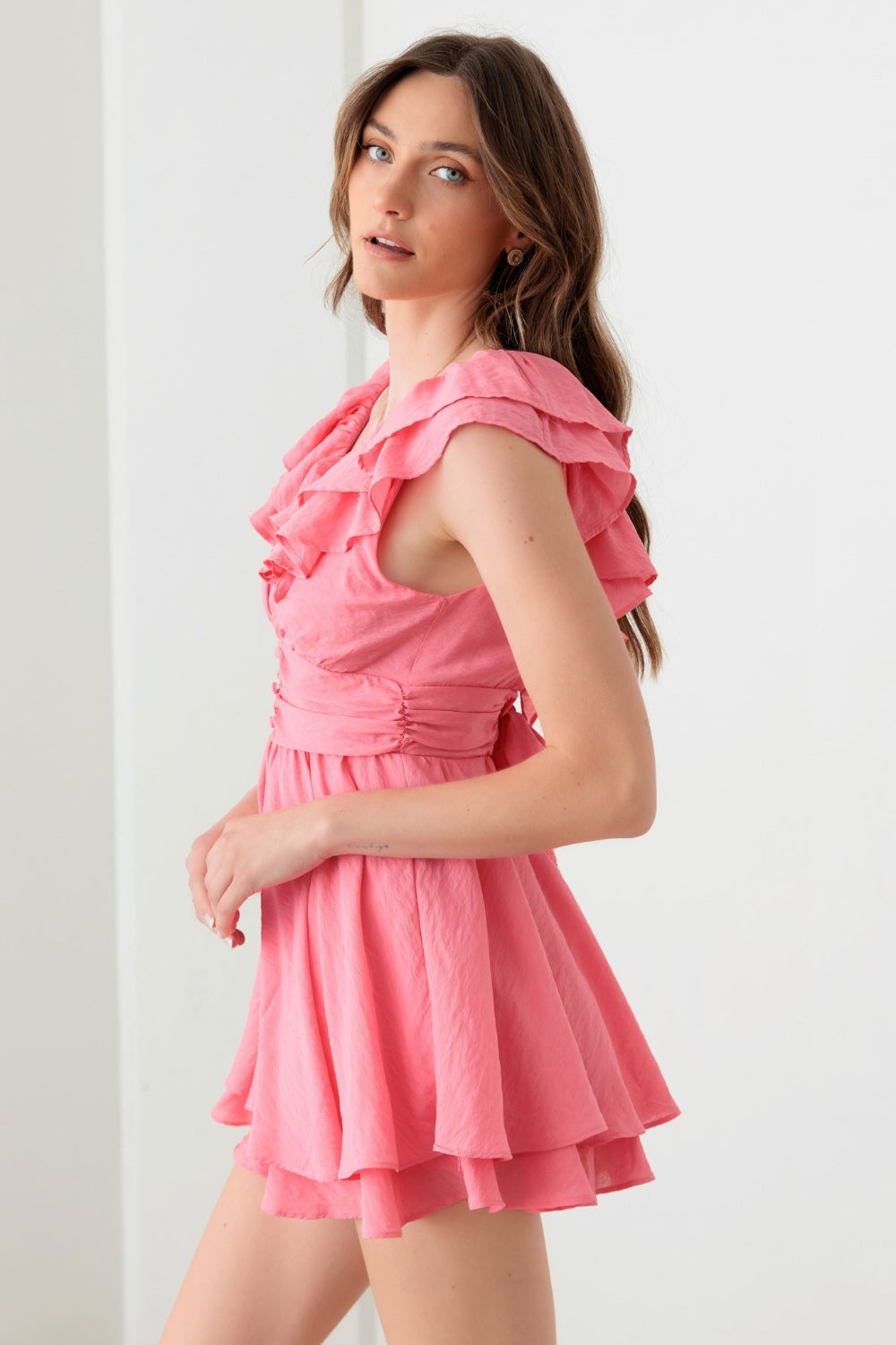 A person wearing a Mustard Seed Tie Back Front Button Ruffled Romper, ideal for a boho-inspired summer wardrobe, stands in front of a plain white background.