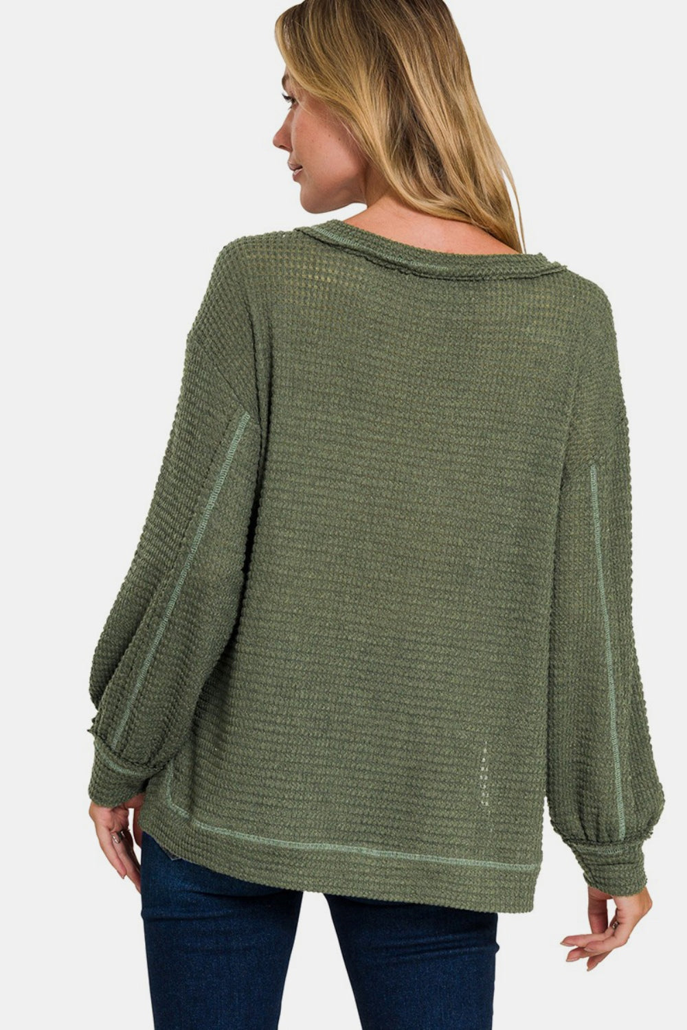 A person wearing the Zenana Exposed Seam Side Slit Long Sleeve Top in textured green, paired with blue jeans, stands against a plain background.