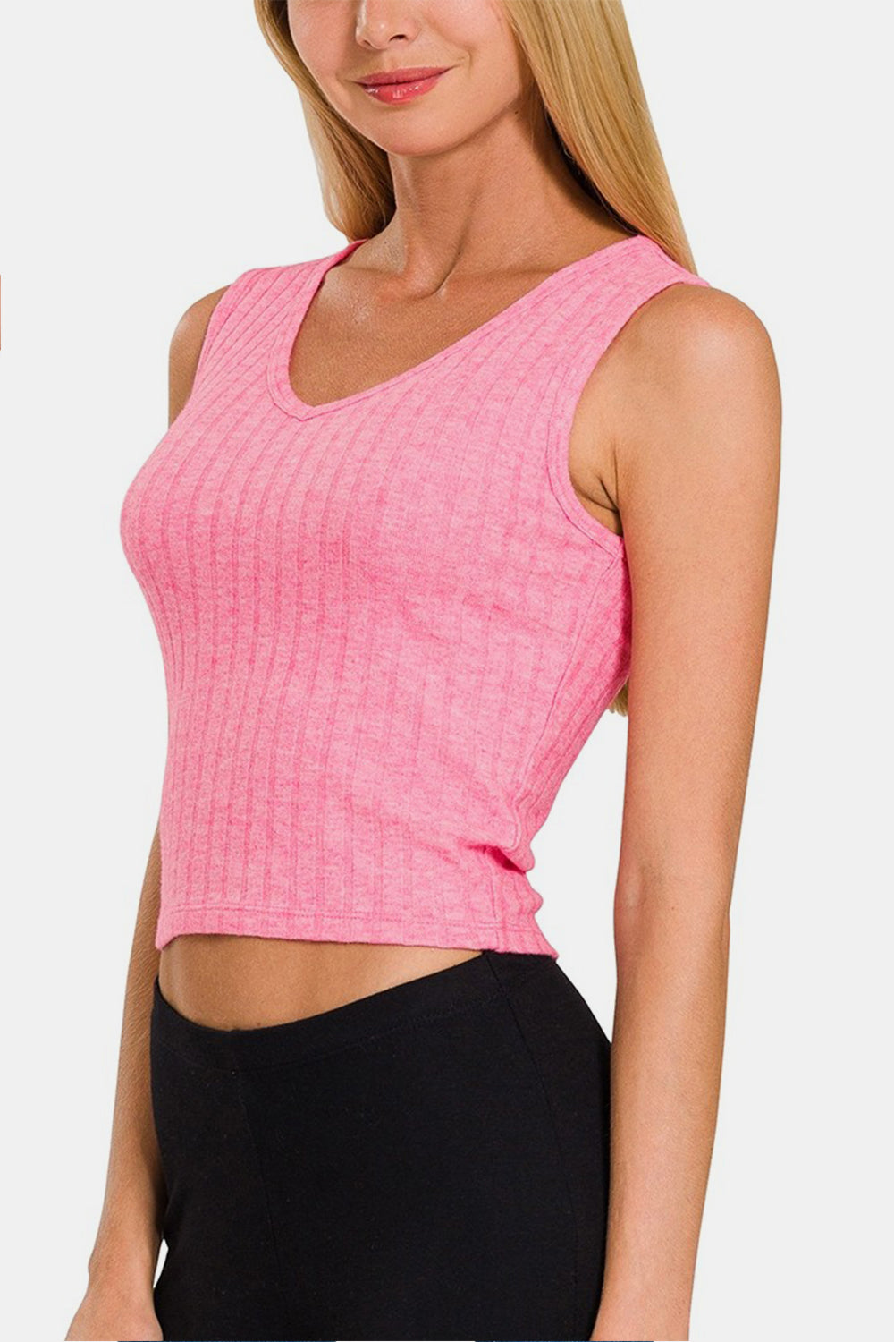 A person wearing a fashionable Zenana Ribbed Cropped Tank in pink, paired with black pants, stands against a plain background.