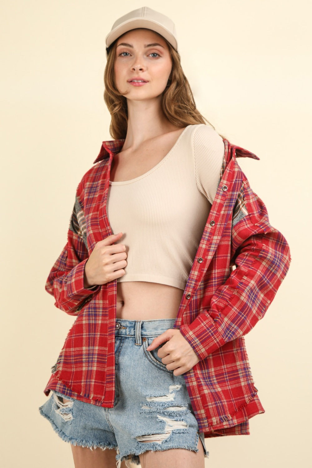 A woman wearing a VERY J Contrast Plaid Raw Detail Shirt, blue denim shorts, and a beige cap poses against a plain background.