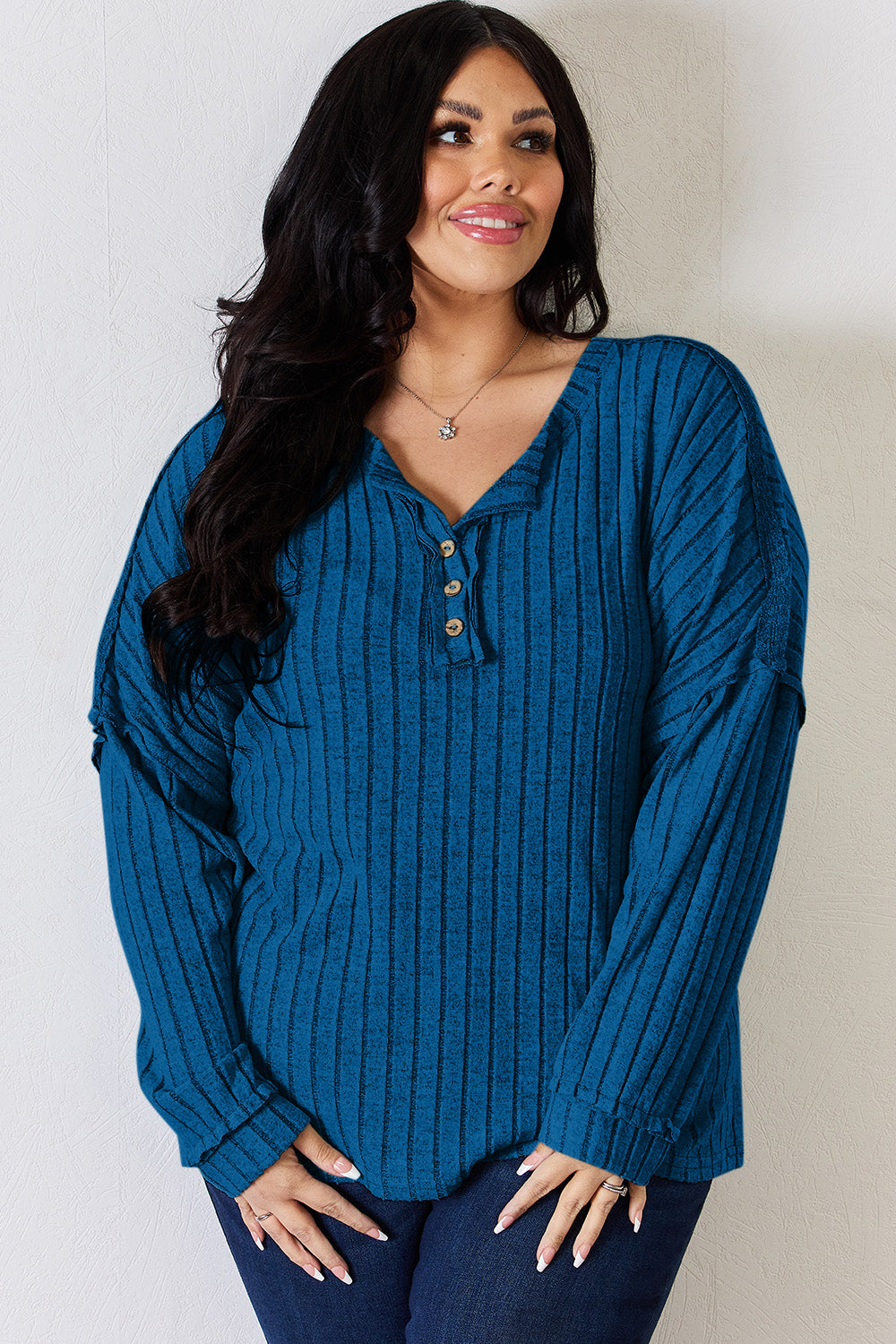 A woman with long, wavy blonde hair wears a slightly stretchy, textured Basic Bae Full Size Ribbed Half Button Long Sleeve T-Shirt in pink, standing against a neutral backdrop.