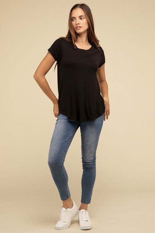 A person with long hair is wearing a blue Flowy Round Hem Rayon Short Sleeve Top and black pants, standing against a plain beige background.