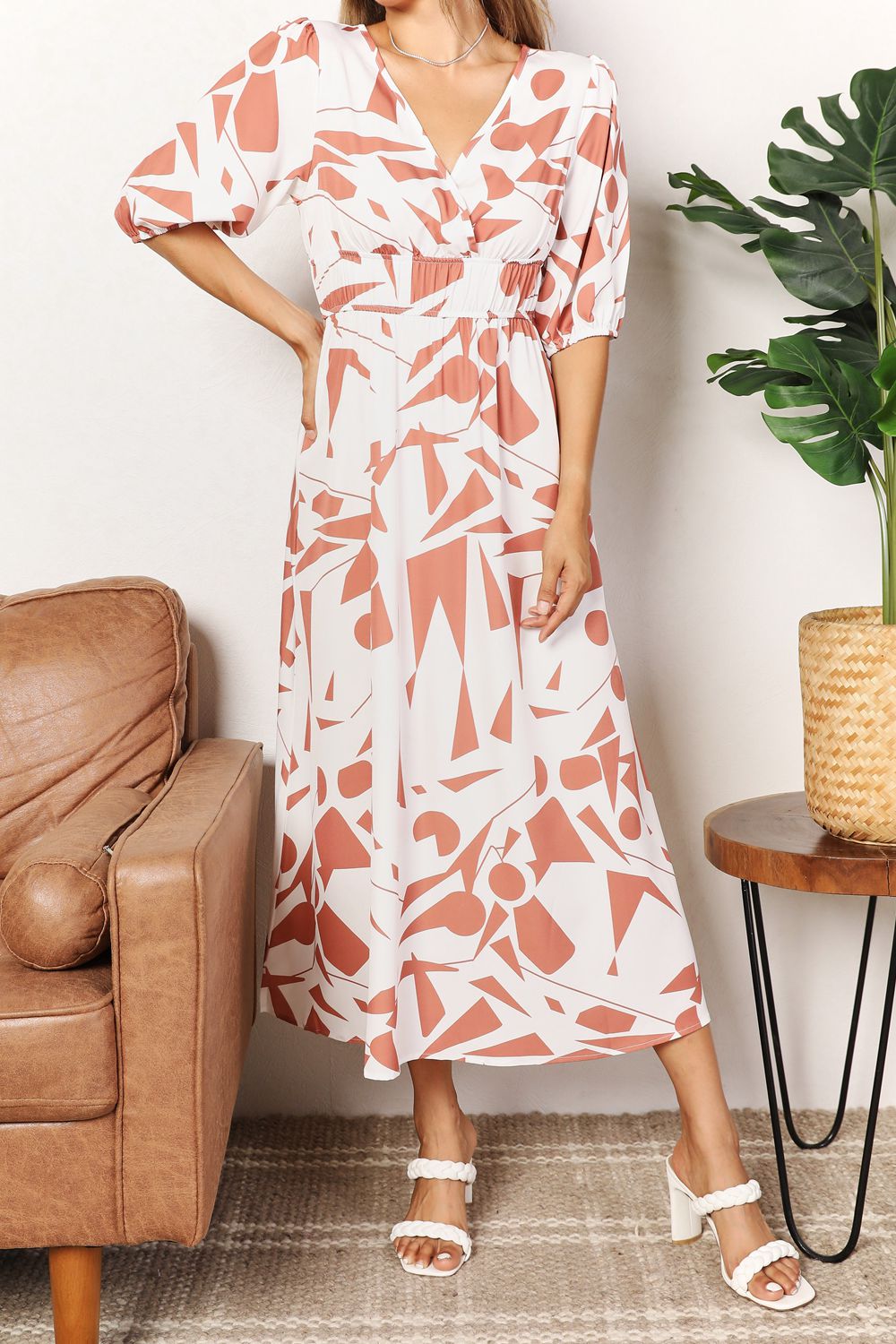 A person in a Printed Surplice Balloon Sleeve Dress stands near a brown chair and a round table with a potted plant.