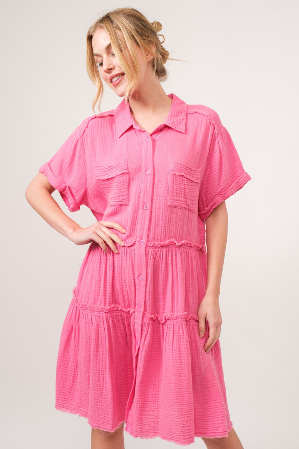 A person wearing the And The Why Full Size Raw Edge Washed Tiered Shirt Dress and light brown heels stands with hands on hips against a neutral background.