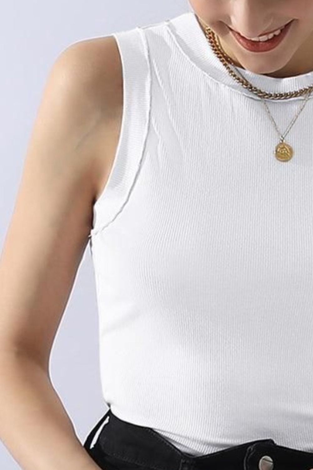 A person wears a versatile and comfortable Ninexis Ribbed Round Neck Tank in black, paired with black jeans and gold jewelry, smiling against a white background.