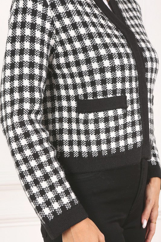 A woman dressed in the Black Check Knitted Jacket, featuring snap buttons and functional pockets, complemented by black pants, stands against a white background.