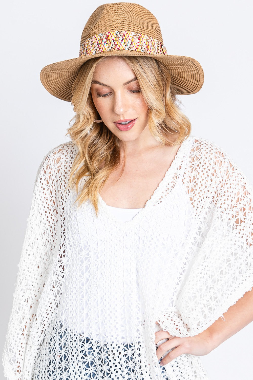 A woman in a chic summer outfit wears the Fame Contrast Detail Wide Brim Straw Hat, featuring a multicolored band. The contrast detail of her white crocheted top enhances her sophistication as she gazes down contemplatively.