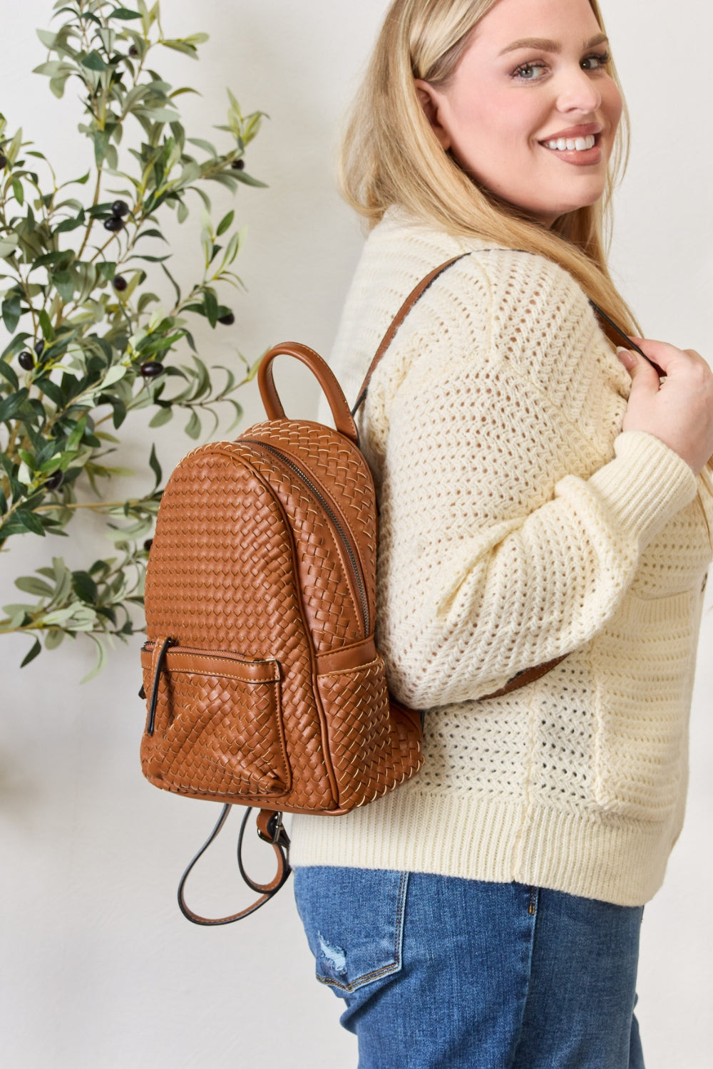 A person wearing a cream sweater and jeans is carrying the SHOMICO PU Leather Woven Backpack in brown.