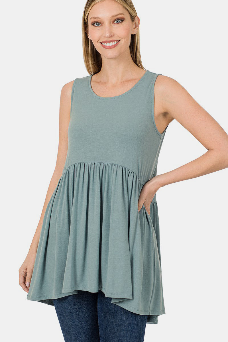 A person wearing a Zenana Round Neck Wide Strap Babydoll Top in light green with blue jeans stands while smiling.