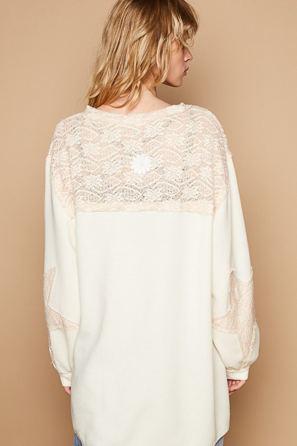 A person with long hair stands against a plain beige background, wearing the POL Round Neck Long Sleeve Crochet Patches Top, which features a loose-fitting white and beige lace pattern.