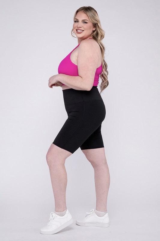 Against a plain background, a person showcases the Plus Athletic High Rise Biker Shorts in coral, crafted from high-quality athletic fabric and paired with a pink top.