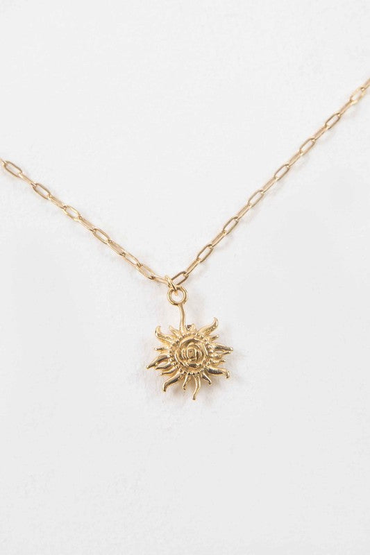 The Helio Charm Necklace is a piece made with 14k gold plating, featuring a sun-shaped pendant with a smiling face against a light backdrop.