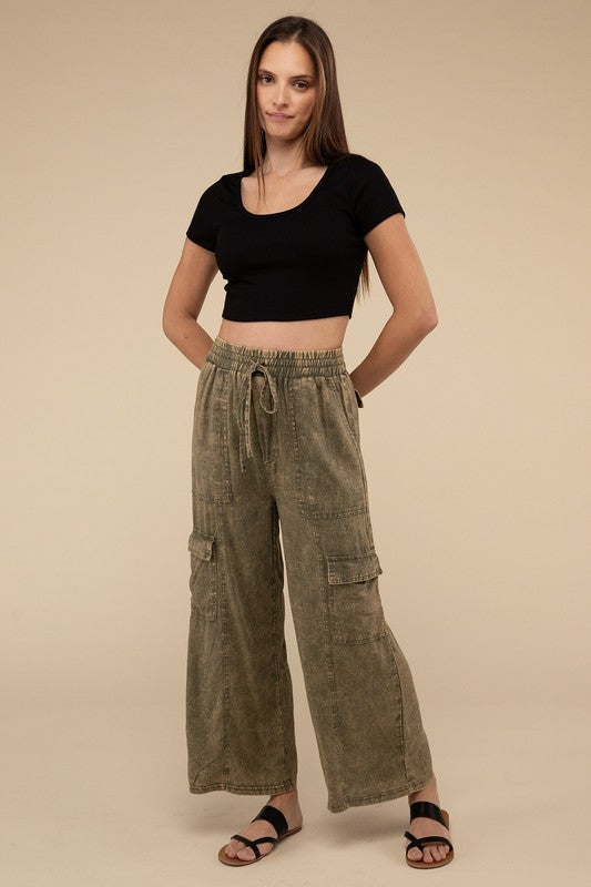 A person wearing Washed Linen Elastic Band Waist Cargo Pants in light blue with hands in pockets, paired with a white top and open-toe sandals. The background is plain beige.