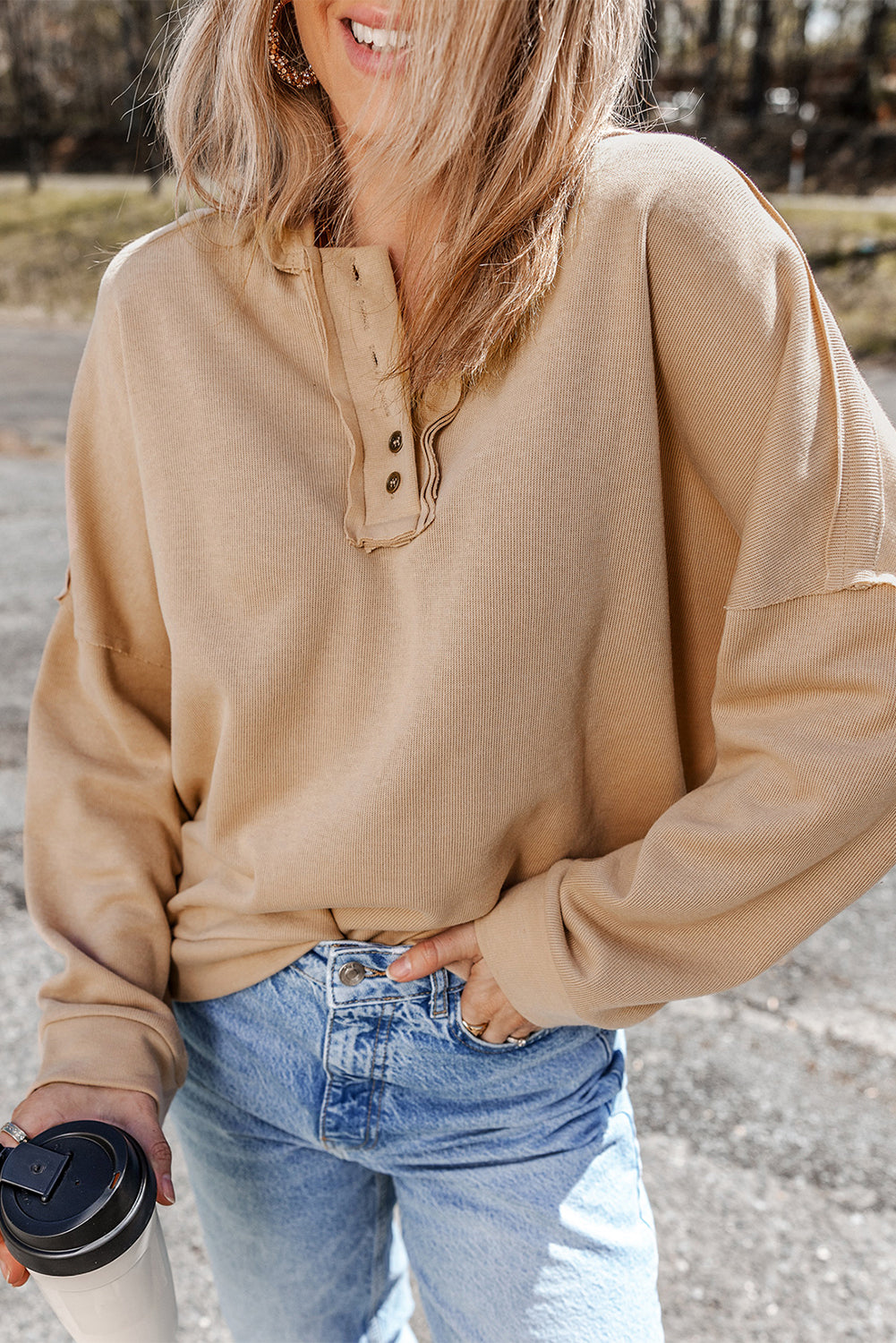 Person wearing a Khaki Casual Button Solid Patchwork Trim Hoodie and blue jeans is standing outdoors holding a white tumbler. The individual's blonde hair is partially visible from behind.