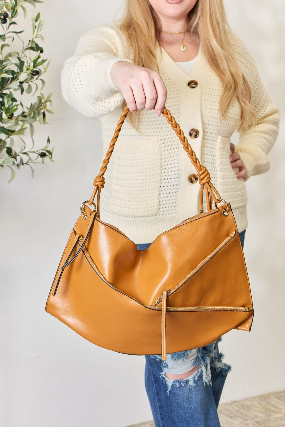 A person in a cream sweater holds a medium-size SHOMICO Zipper Detail Shoulder Bag with gold metal zipper pockets.