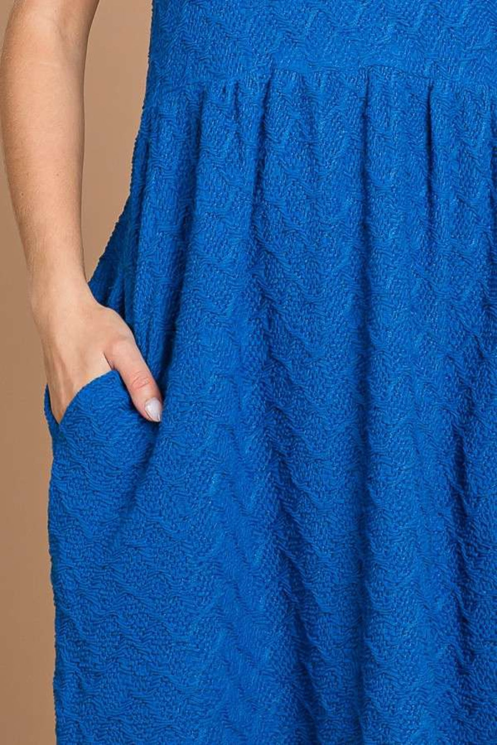 Against a plain brown backdrop, an individual is styled in a Culture Code Texture Round Neck Short Sleeve Dress with Pockets, exuding elegance and flair with its blue textured fabric and chic short puff sleeves.