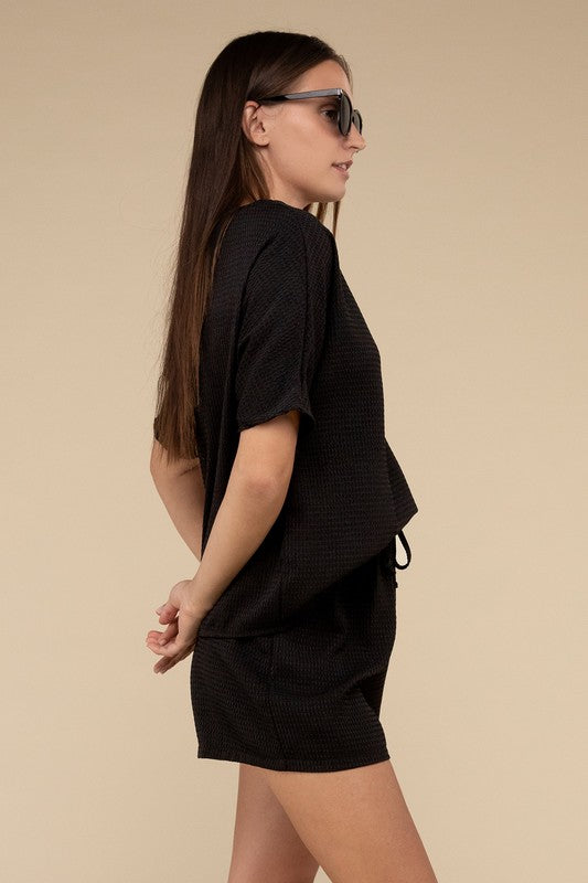 Clad in the Waffle Round Neck Top and Short Set paired with black sunglasses, a person stands against a plain beige background, highlighting the non-stretch polyester fabric.