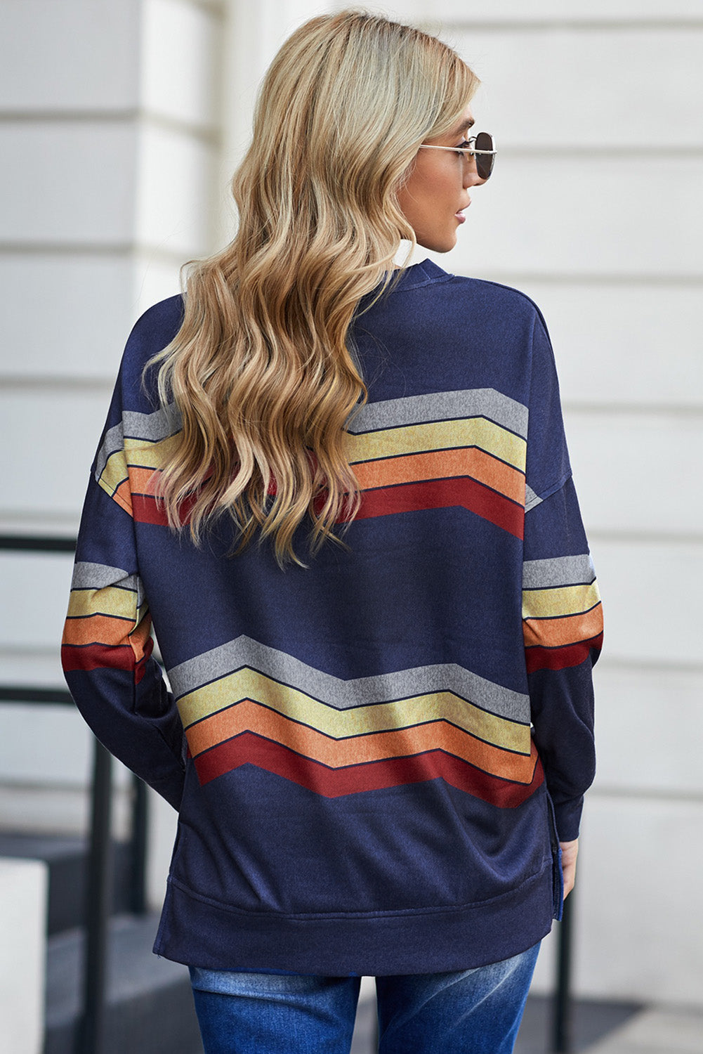 A person with long, wavy blonde hair wearing glasses and a Blue Color Block Classic Sweatshirt stands with their back facing the camera.