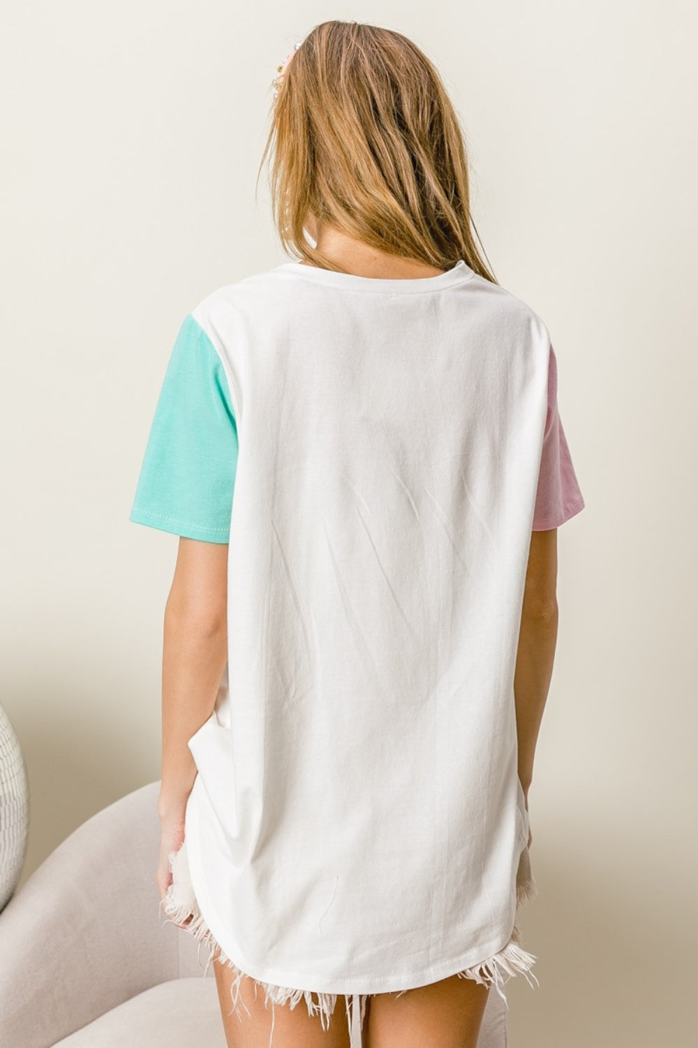 A woman wearing a BiBi Letter Patch V-Neck Color Block Short Sleeve T-Shirt, which features "Lake Days" printed on it, sits on a chair. She holds the shirt's sleeves and wears a headband and earrings.