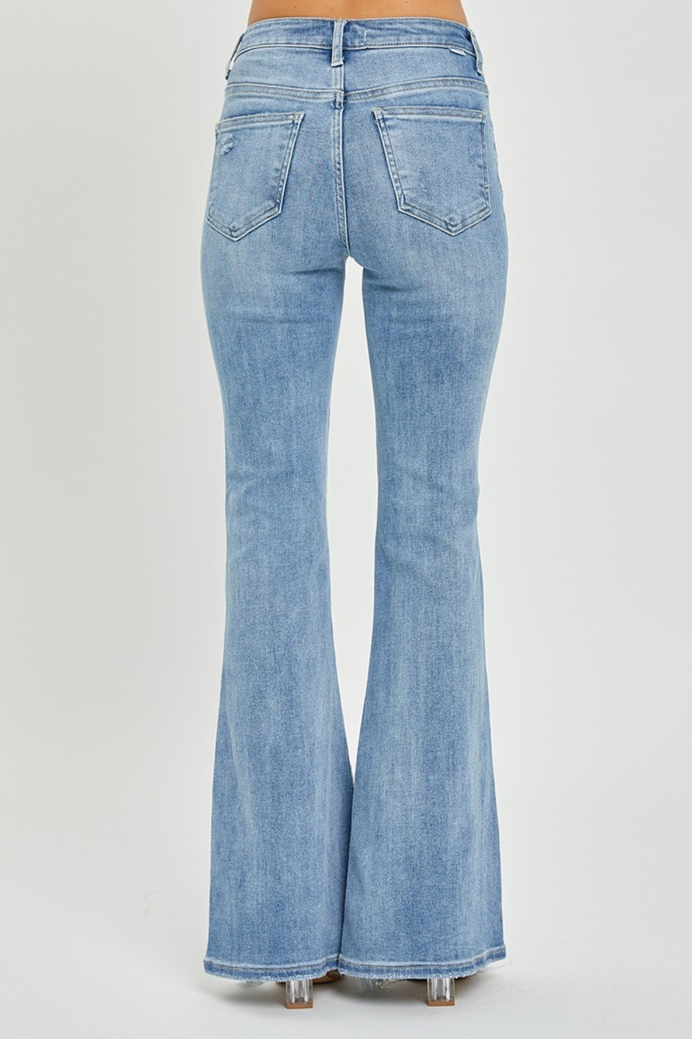 A person wearing the Risen Full Size High Rise Frayed Hem Flare Jeans in light blue with distressed details.